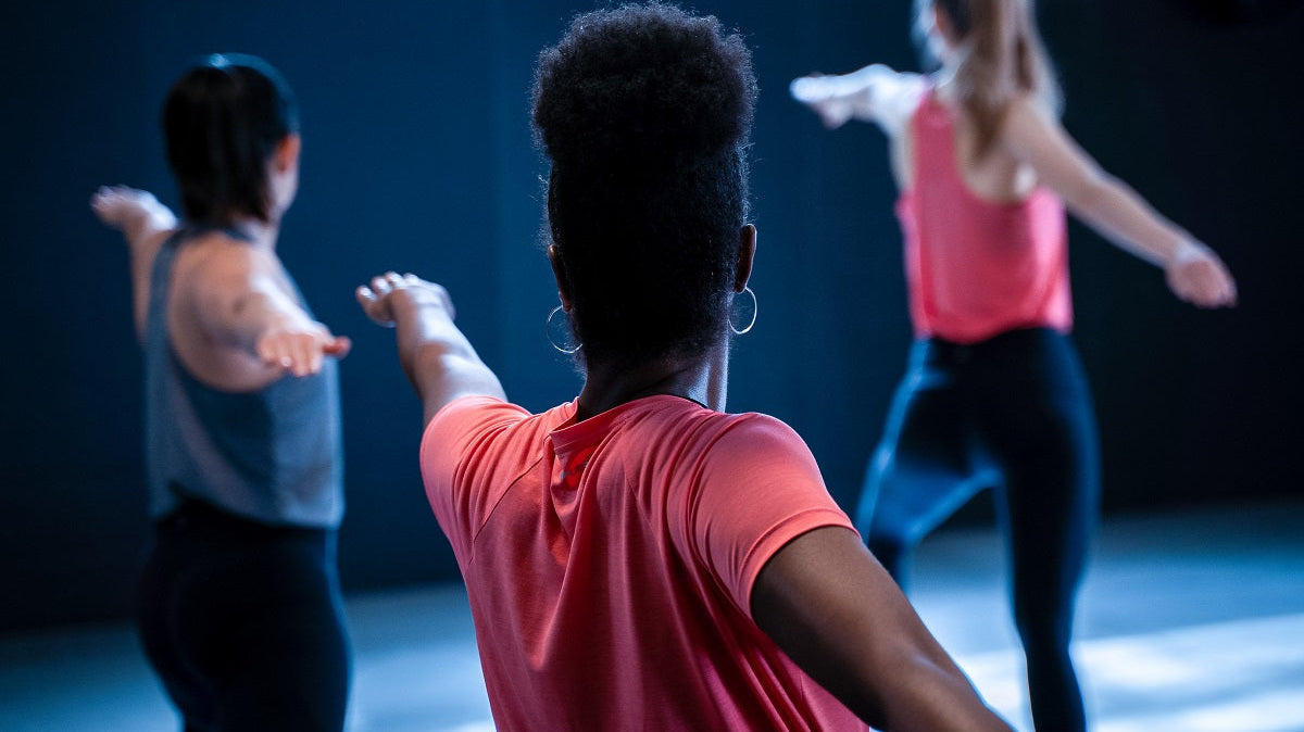 Dancers stretching in a studio wearing coral and white tops.