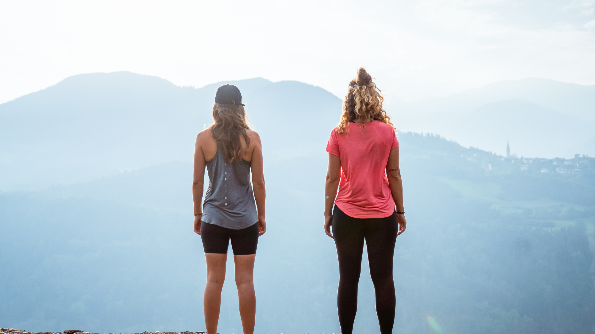 Two women looking out over misty hills, one in a grey tank top and one in a pink T-shirt.