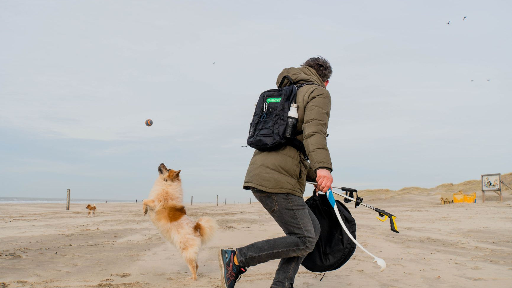 Plogger Daan Strang playing with his dog on a beach while collecting litter.