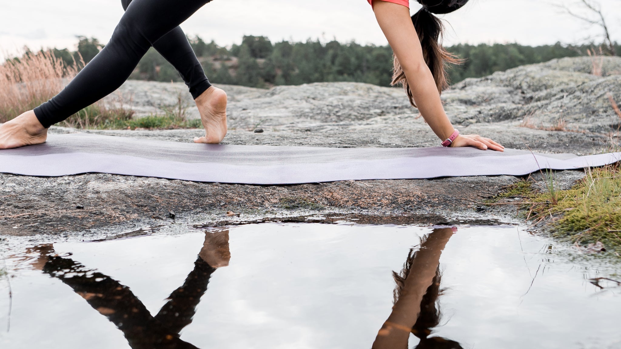 Woman doing a yoga wheel pose on a mat by a lake, reflected in the water.