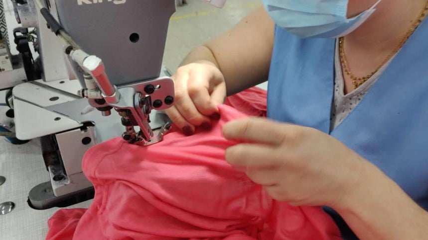 Seamstress sewing a coral garment at a factory sewing machine.