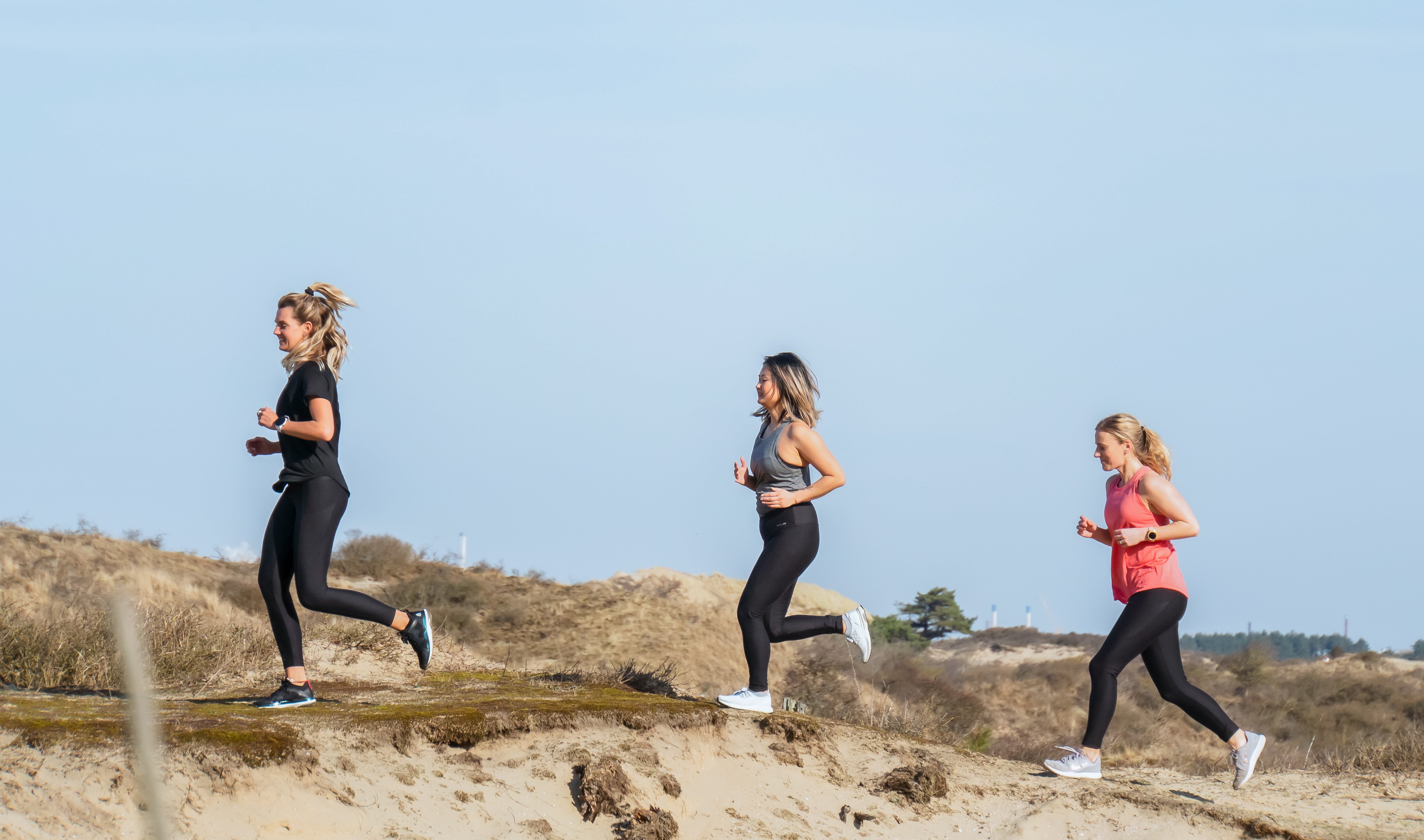 Three runners in Tripulse activewear running over coastal dunes.