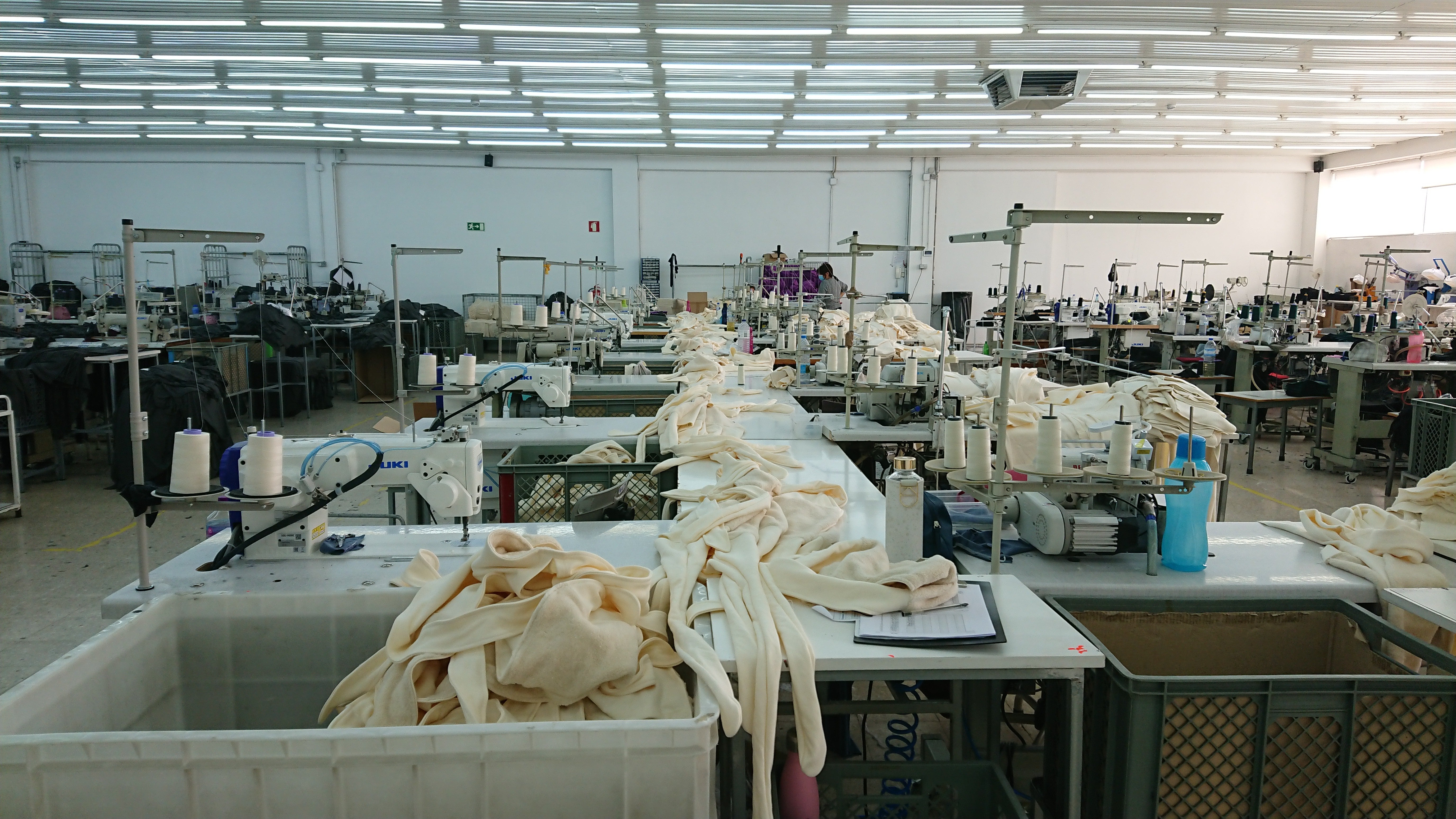 Garment factory floor with sewing stations and cut fabric pieces.