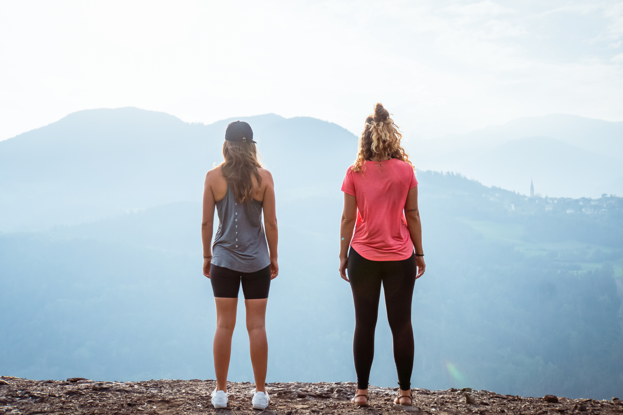 Two women looking out over misty hills, one in a grey tank top and one in a pink T-shirt.