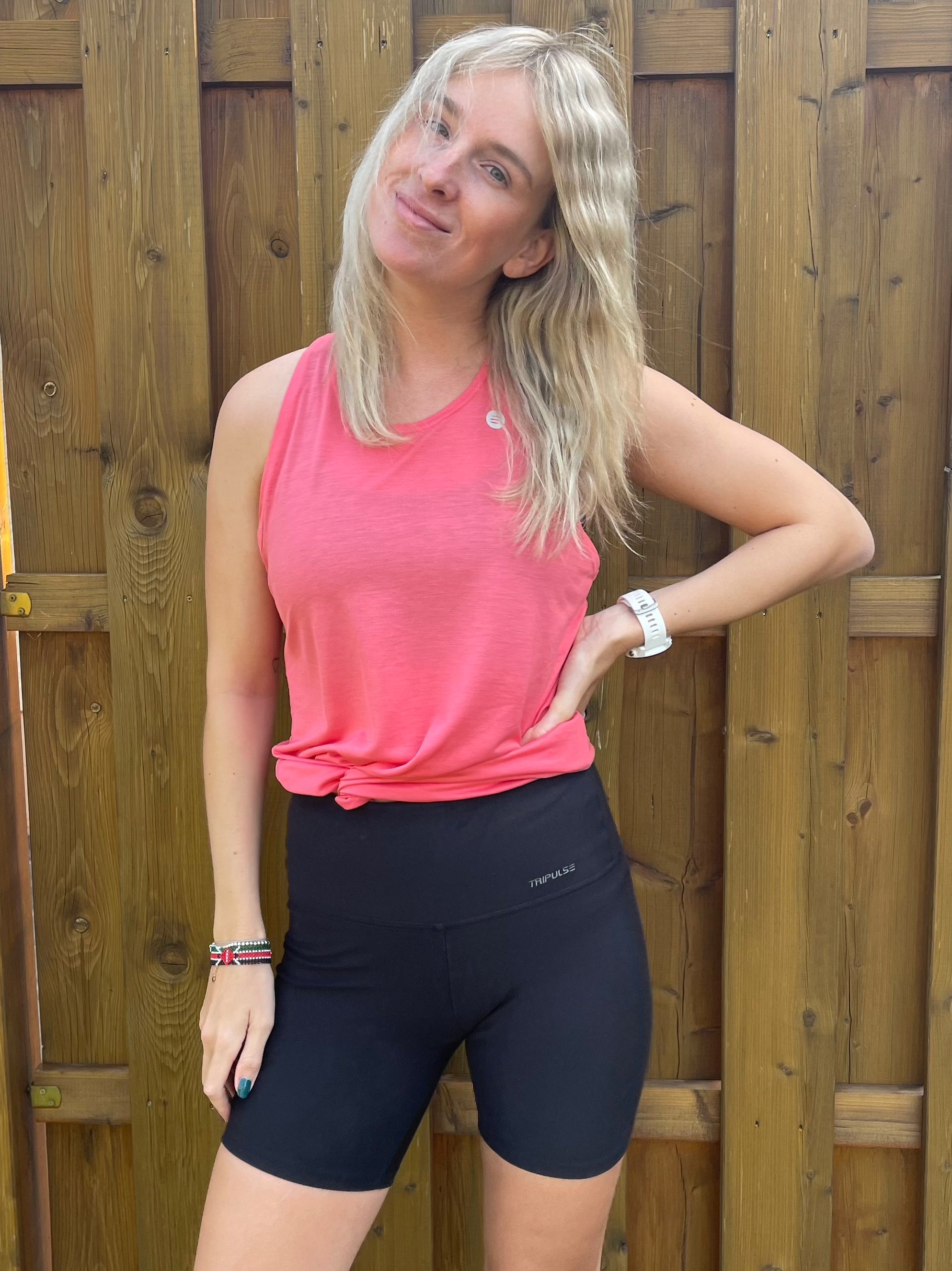Nele Dork from Runnerfeelings posing in a pink tank top and black shorts against a wooden wall.