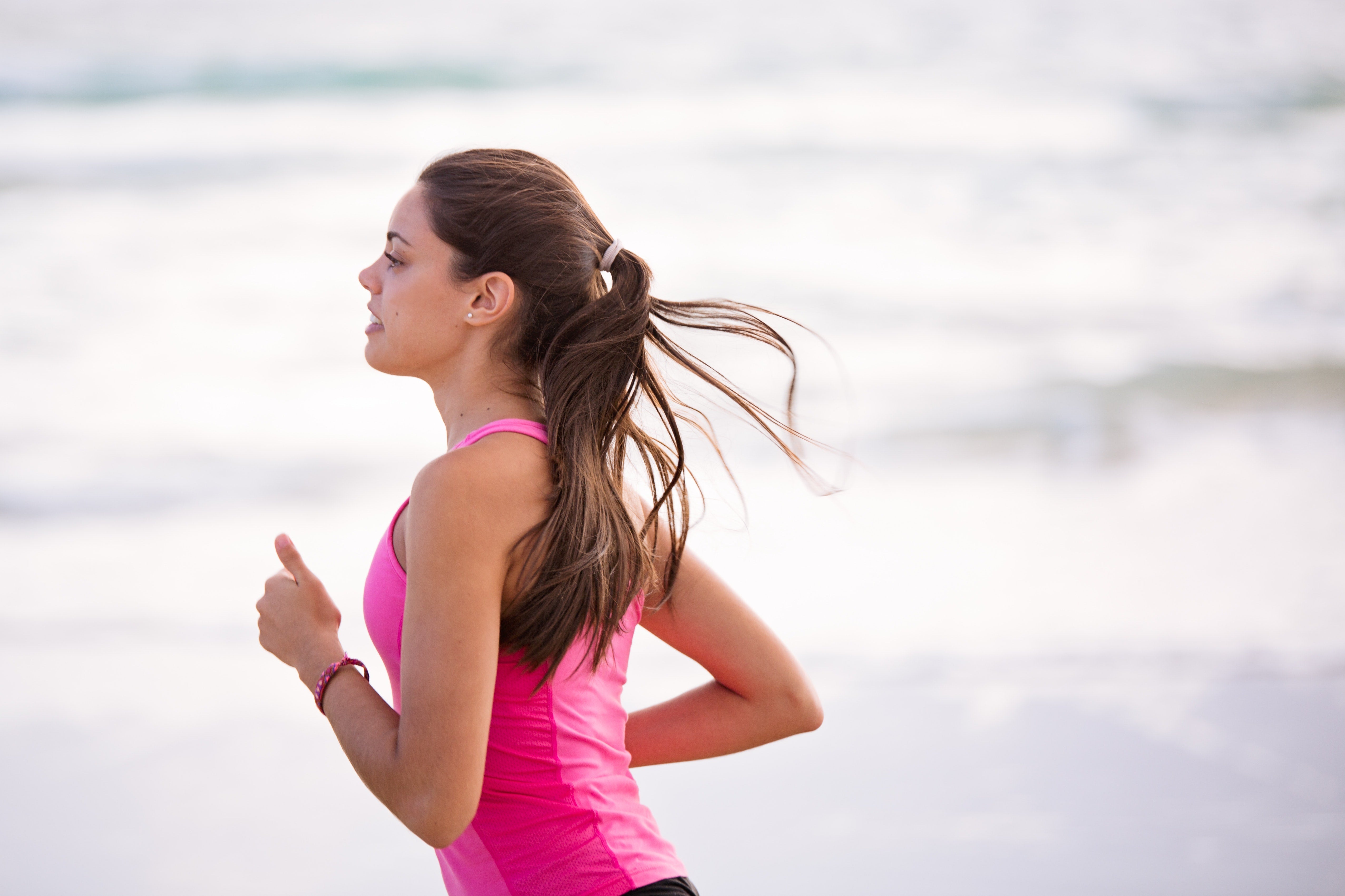 Woman running along the shoreline in a pink tank top.