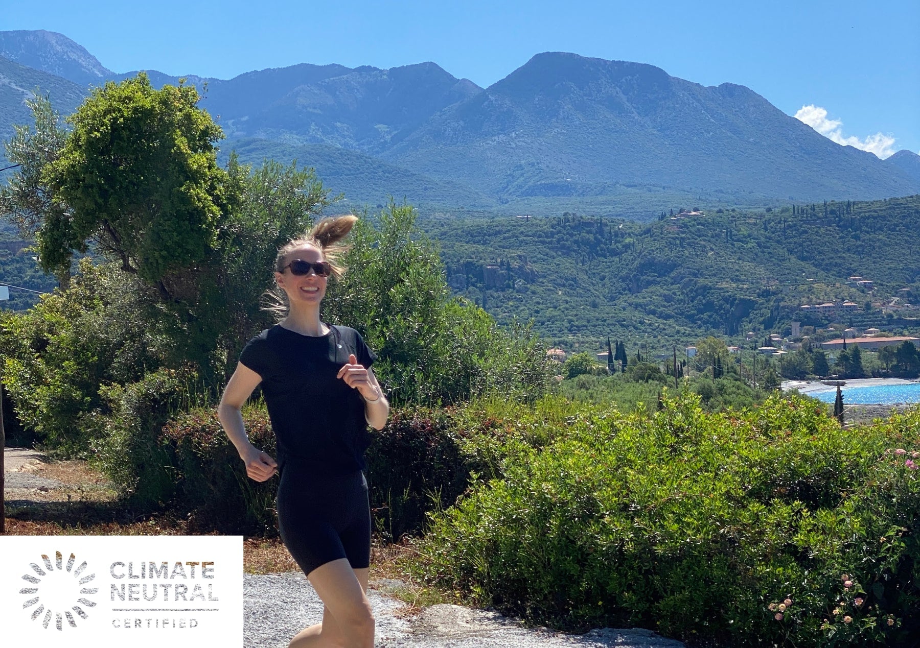 Woman running on a sunny mountain trail with the Climate Neutral Certified label.